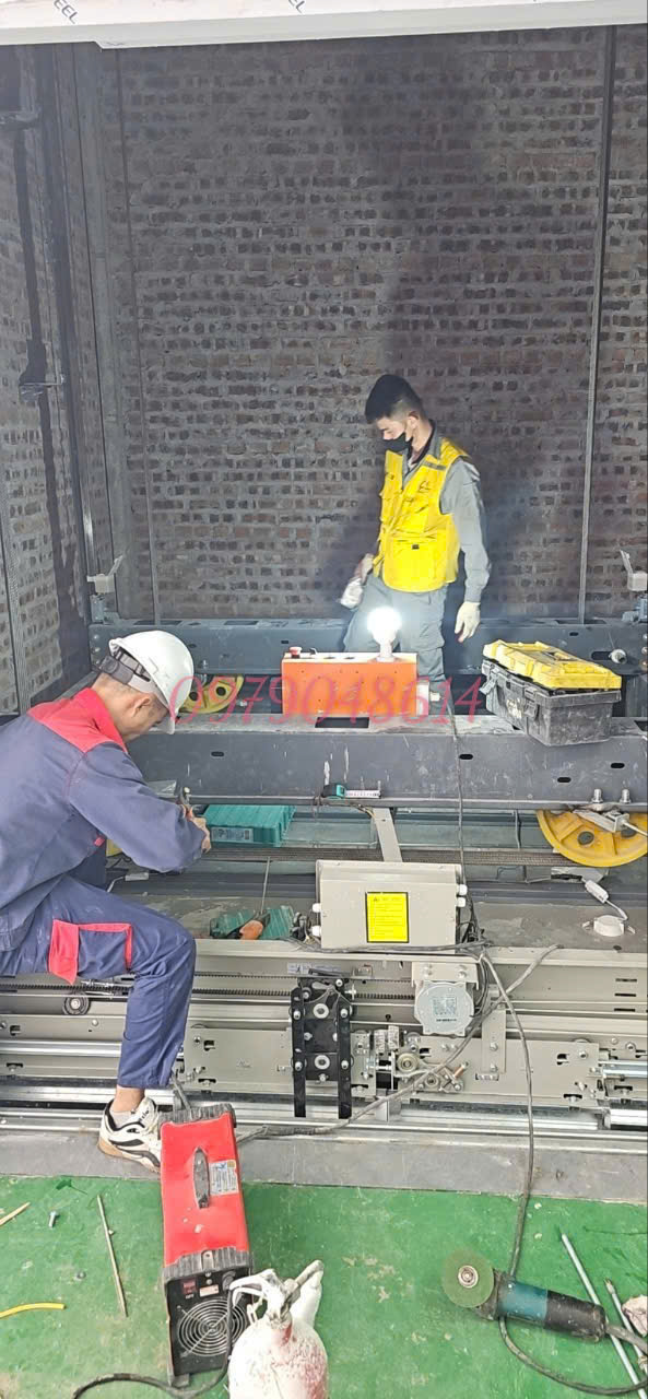 Kỹ thuật viên đang lắp đặt hệ thống máy kéo cửa thang máy trong giếng thang xây gạch